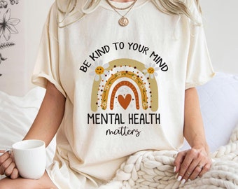 May include: A white t-shirt with a rainbow graphic and the text "Be kind to your mind Mental health matters". The rainbow is decorated with daisies and a heart.
