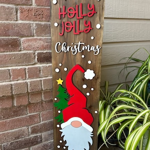 May include: Wooden Christmas sign with the text "Have a Holly Jolly Christmas" in white lettering. A red and white gnome with a green Christmas tree is on the sign.