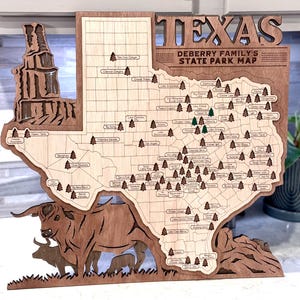 May include: A wooden Texas state park map with the text "TEXAS DEBERRY FAMILY'S STATE PARK MAP". The map features a grid, tree icons, and the names of state parks. A bull and two calves are carved at the bottom.