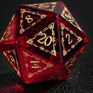 May include: A red, twenty-sided die with gold numbering and accents. The numbers are displayed in a triangular shape. The die is made of a translucent material, allowing light to pass through. The die is used for tabletop role-playing games.