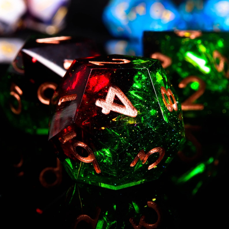 May include: A green and red polyhedral dice with copper-coloured numbers. The dice has a 4 on one side and a 3 on another side.