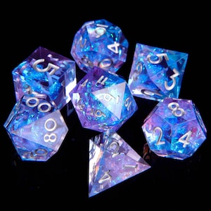 May include: A set of seven iridescent dice in shades of blue and purple with silver numbers. The dice are made of a clear material with a glittery finish.