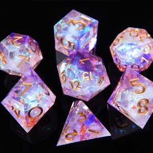 May include: Set of seven iridescent purple and gold dice with a glittery finish. The dice are shaped like various geometric shapes, including a cube, a pyramid, and a dodecahedron. The numbers on the dice are in gold.