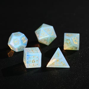 May include: Five iridescent dice in various shapes: a d20, d12, d6, d4, and d8. The dice are a pale blue with gold numbering and decorative accents. The dice are designed for tabletop role-playing games.