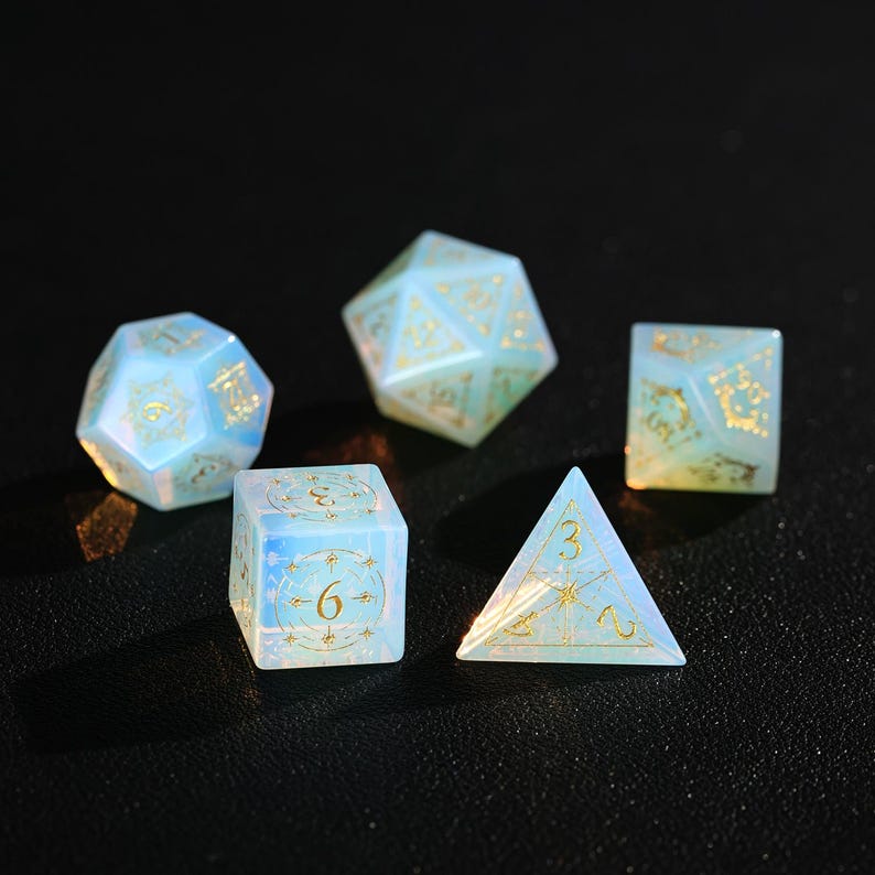 May include: Five iridescent dice in various shapes: a d20, d12, d6, d4, and d8. The dice are a pale blue with gold numbering and decorative accents. The dice are designed for tabletop role-playing games.