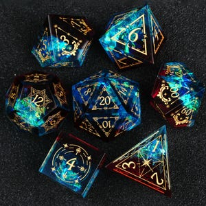 May include: A set of seven polyhedral dice featuring a translucent blue and red resin base with embedded iridescent green and blue foil flakes. Each die is marked with intricate gold-colored filigree numbering and geometric star patterns.