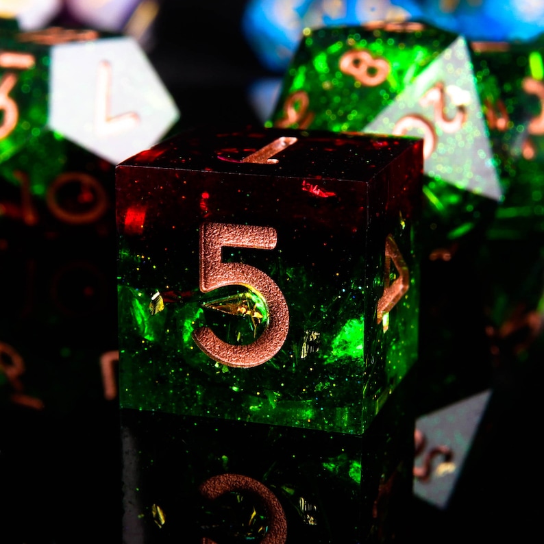 May include: A close-up of a green and red dice with copper-coloured numbers. The dice has a glittery finish and is showing the number five.