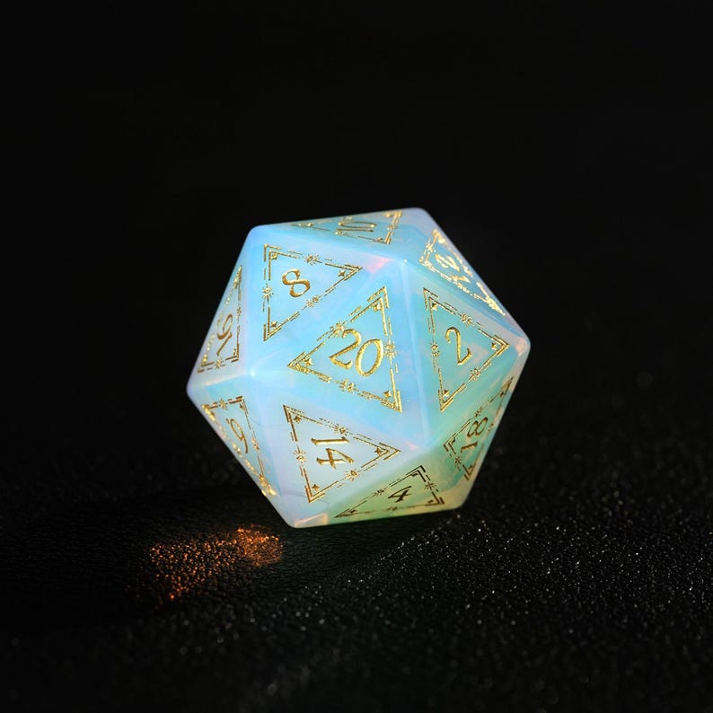 May include: A twenty-sided die with a pearlescent, opalescent finish. The die features gold-colored numerals and decorative accents. The numbers are clearly visible against the light blue and white background. This gaming accessory is perfect for tabletop games.