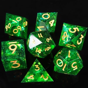 May include: Set of seven green and gold dice with glitter embedded in the plastic. The dice are numbered 1 through 6 and 10 through 20.
