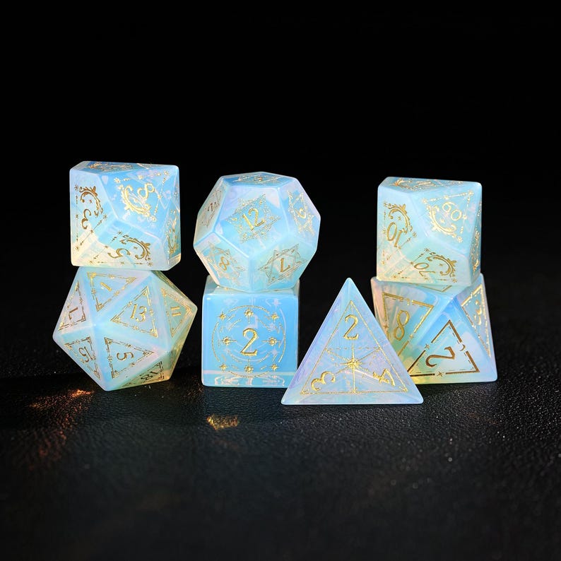 May include: A set of seven opalescent dice in various geometric shapes. The dice are a pale blue with gold numbering and decorative flourishes. The dice are for role-playing games.