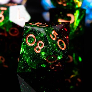 May include: A green and red iridescent d20 dice with copper-coloured numbers. The dice has a glittery finish.