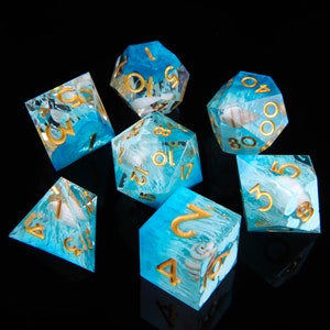 May include: Set of seven blue and white dice with gold numbers and swirls. The dice have a seashell design inside.