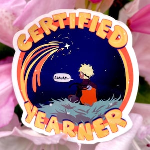 Könnte beinhalten: Ein Aufkleber mit den Worten "CERTIFIED YEARNER" in Orange und Gelb. Der Aufkleber zeigt eine Cartoon-Illustration einer Figur, die auf einen Sternschnuppen in einem Nachthimmel blickt. Die Figur trägt ein orange-schwarzes Outfit. Das Wort "Sasuke..." steht in einer Sprechblase.