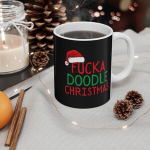 Può includere: Tazza in ceramica nera con la scritta "FUCK A DOODLE CHRISTMAS" in rosso e verde, sormontata da un cappello di Babbo Natale. La tazza è riempita con un liquido scuro e ha un manico bianco.
