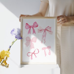 May include: A framed print with a white background featuring six pink watercolor bows of varying sizes and shapes.