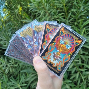 May include: A collection of six cassette tapes with colorful designs. The tapes feature the band "Dead & Company" and various images, including a phoenix, a cityscape, and a psychedelic pattern.