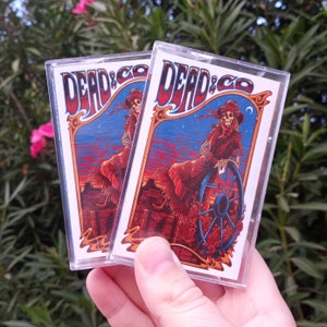 May include: Two cassette tapes with a colorful graphic design featuring a skeleton figure in a cowboy hat and the text "Dead & Co."