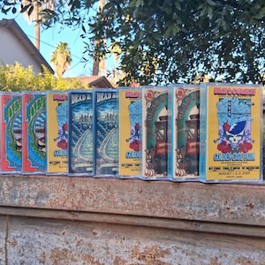 May include: A row of vintage cassette tapes with colorful artwork and the text "DEAD & COMPANY GOLDEN GATE PARK AUGUST 1, 2, 3, 2025". The tapes feature various designs, including a skull, train, and city skyline.