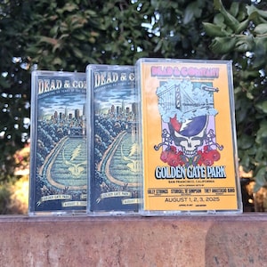 May include: Three cassette tapes featuring artwork for Dead & Company concerts. The tapes have colorful designs, including cityscapes and the band's iconic skull logo. The text on the tapes includes "Golden Gate Park" and concert dates.