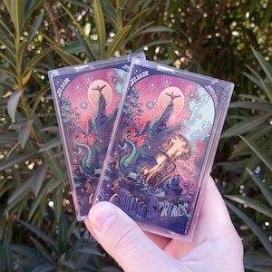 May include: Two clear cassette tapes with colorful artwork featuring a green alligator with a gold trumpet. The text on the tape reads "Billy Strings" and "2.25.2022".
