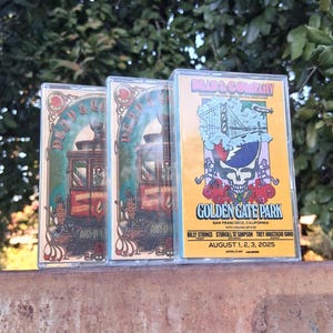 May include: Three cassette tapes featuring concert artwork for Dead & Company at Golden Gate Park in San Francisco. The tapes have a colorful design with a skull, roses, and the Golden Gate Bridge. The concert dates are August 1, 2, and 3, 2025.