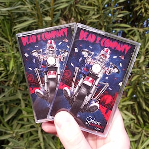 May include: Two cassette tapes with a colorful graphic of a skeleton riding a motorcycle. The text on the tape says "Dead & Company" and "Sphere Las Vegas 8.22.24".