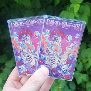May include: Two cassette tapes with the text "Dead & Company" and "May 15, 2023 Sphere Las Vegas". The artwork features a skeleton with a floral crown, surrounded by bears and flowers, in shades of purple, pink, and blue.