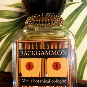 May include: A clear glass bottle with a black and gold cap. The bottle has a label that says "Backgammon Men's botanical cologne".