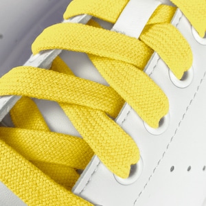 Può includere: Primo piano di scarpe da ginnastica bianche con lacci gialli. I lacci sono intrecciati a forma di croce.