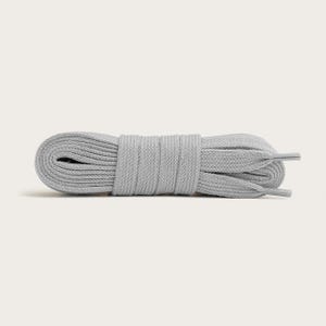 Può includere: Un fascio arrotolato di lacci delle scarpe grigio chiaro. I lacci sono piatti e realizzati in un materiale tessuto. Le estremità dei lacci sono rifinite con plastica o materiale simile per evitare lo sfilacciamento. Lo sfondo è di un colore neutro uniforme.