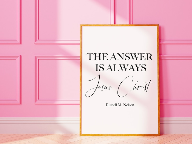 May include: A white framed print with a black and white quote that reads "The answer is always Jesus Christ" by Russell M. Nelson. The print is on a pink wall.
