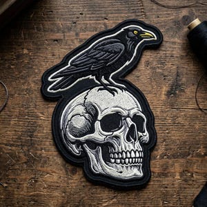 May include: Embroidered patch featuring a black raven perched atop a detailed white skull. The raven has yellow eyes and a yellow beak. The patch is outlined in black and set against a wooden background.