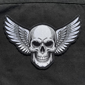 May include: Embroidered patch featuring a detailed white skull with large, stylized wings in shades of gray. The patch is set against a black background, creating a striking contrast. The design is intricate and suitable for jackets or bags.