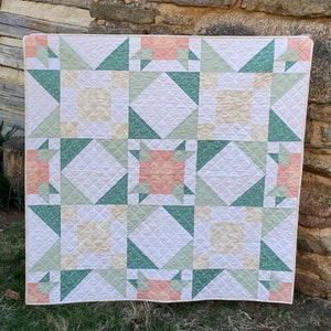 May include: A white quilt with a patchwork design featuring green, pink, and cream squares and triangles. The quilt is quilted with a diamond pattern.