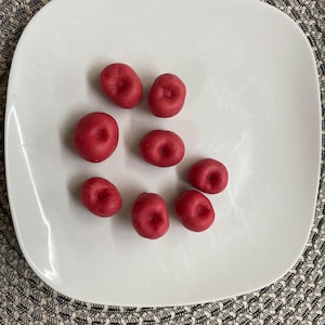 May include: A white plate with eight red candy-coated chocolates arranged in a circle.