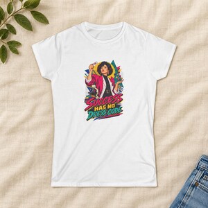 May include: A white short-sleeved t-shirt featuring a colourful graphic print of a person in a pink blazer holding a small card and a molecular model. Below the figure, the text reads SUCCESS HAS NO DRESS CODE in bold, stylised lettering.