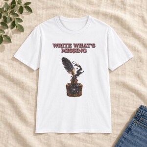Può includere: Una t-shirt bianca a maniche corte con il testo "WRITE WHAT'S MISSING" in un carattere rosso scuro sopra la grafica di una penna d'oca in un calamaio, entrambi riempiti con un motivo a galassia blu scuro con stelle e pianeti.