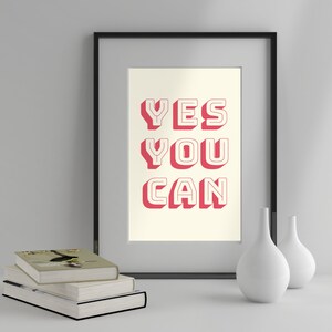 Może przedstawiać: Wydruk w ramie z białym tłem i tekstem "YES YOU CAN" w pogrubionych, czerwonych literach z białym obramowaniem. Wydruk znajduje się w czarnej ramie i leży na białym tle z dwoma białymi wazami.