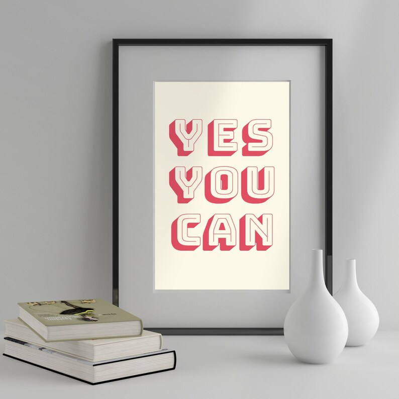 Może przedstawiać: Wydruk w ramie z białym tłem i tekstem "YES YOU CAN" w pogrubionych, czerwonych literach z białym obramowaniem. Wydruk znajduje się w czarnej ramie i leży na białym tle z dwoma białymi wazami.
