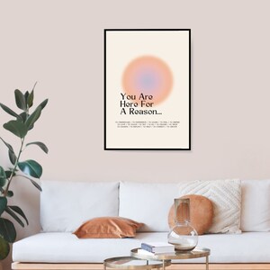 Op de afbeelding: Een motiverende poster met een zwart frame en een lichte achtergrond. De poster heeft een grote, wazige, perzikkleurige cirkel met een blauw centrum. De tekst op de poster luidt "You Are Here For A Reason... To Understand / To Experience / To Learn / To Feel / To Inspire / To Love / To Teach / To Try / To Do / To Choose / To Trust / To Change / To Help / To Connect / To Create."