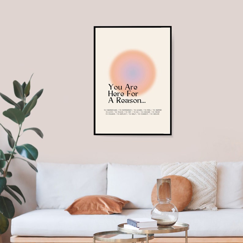 Op de afbeelding: Een motiverende poster met een zwart frame en een lichte achtergrond. De poster heeft een grote, wazige, perzikkleurige cirkel met een blauw centrum. De tekst op de poster luidt "You Are Here For A Reason... To Understand / To Experience / To Learn / To Feel / To Inspire / To Love / To Teach / To Try / To Do / To Choose / To Trust / To Change / To Help / To Connect / To Create."