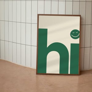May include: A framed art print with the word "hi" in dark green block letters. The "h" and "i" are large, with a cream-colored background. A green smiley face is above the "i". The frame is a dark wood color.