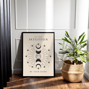 May include: A black framed poster with a beige background. The poster features a black and white illustration of a sun and moon with the text "Let your intuition be your guide".