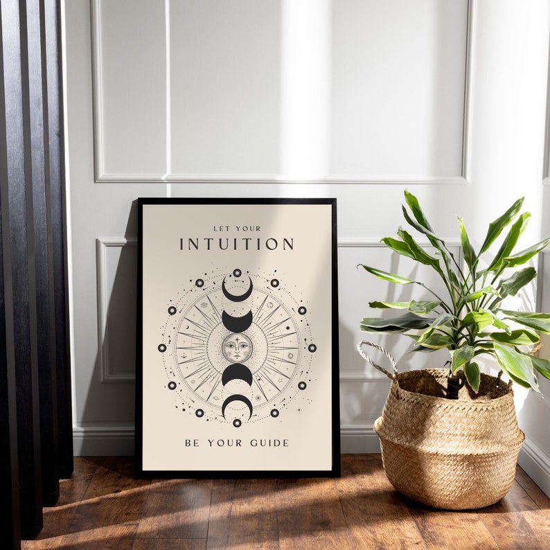 May include: A black framed poster with a beige background. The poster features a black and white illustration of a sun and moon with the text "Let your intuition be your guide".