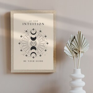 May include: A beige framed print with a black and white illustration of a sun and moon phases with the text "Let your intuition be your guide".