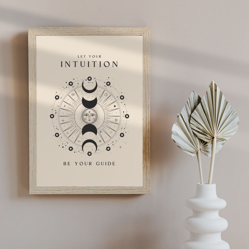 May include: A beige framed print with a black and white illustration of a sun and moon phases with the text "Let your intuition be your guide".