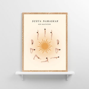 May include: A printable poster with a beige background and a brown wood frame. The poster features a circle with a stylized sun in the center and a woman in various yoga poses around the circle. The text "SURYA NAMASKAR SUN SALUTATION" is at the top of the poster.