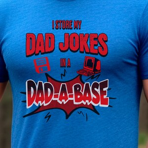 May include: A blue t-shirt with a red and white graphic that says "I store my dad jokes in a dad-a-base". The graphic features a floppy disk and a retro computer.