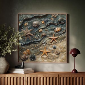 May include: A framed artwork depicting a beach scene with starfish, seashells, and sand. The artwork features a textured, three-dimensional effect with shades of blue, tan, and brown. The frame is a light brown color.