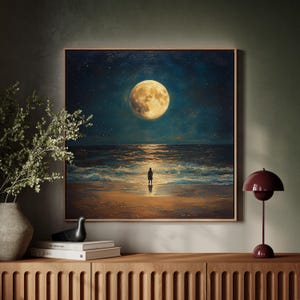 May include: A framed painting depicts a person standing on a beach at night, gazing at a large, bright moon. The sky is dark blue with stars, and the ocean waves reflect the moonlight. The artwork has a warm, inviting color palette.